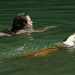 Woman and Dog Swimming in Green Water