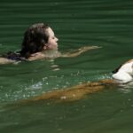 Woman and Dog Swimming in Green Water
