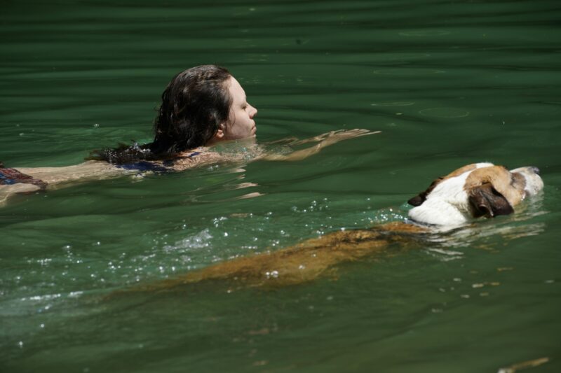 Woman and Dog Swimming in Green Water